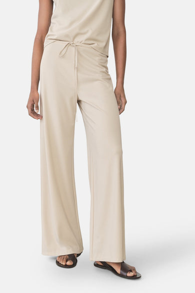 Pantalon beige de MANGO, ample et fluide, avec une taille nouée et porté avec des sandales en cuir.
