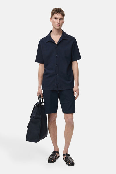 Short bleu foncé de MANGO, porté avec une chemise boutonnée et des sandales en cuir tressé.