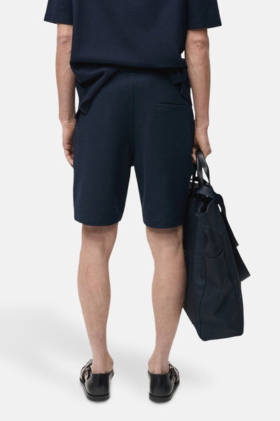 Short bleu foncé de MANGO, avec une poche arrière et porté avec un t-shirt assorti et des sandales noires.