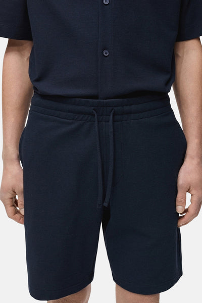 Donkerblauwe korte broek van MANGO, met trekkoord en mesh-textuur, gedragen met een bijpassend overhemd.