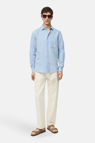 Chemise à manches longues bleue de MANGO, portée avec un pantalon crème et des sandales marron.