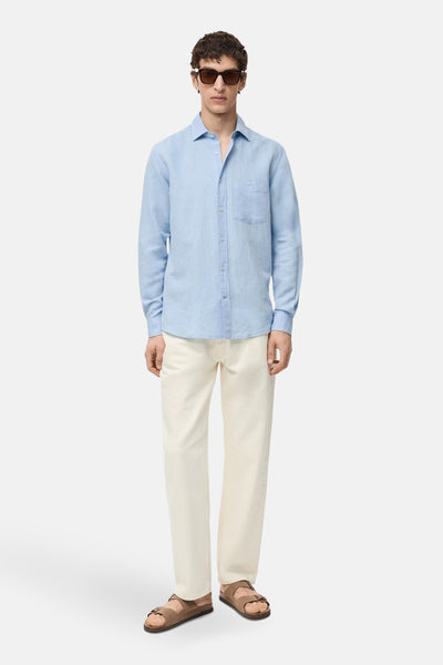Chemise à manches longues bleue de MANGO, portée avec un pantalon crème et des sandales marron.