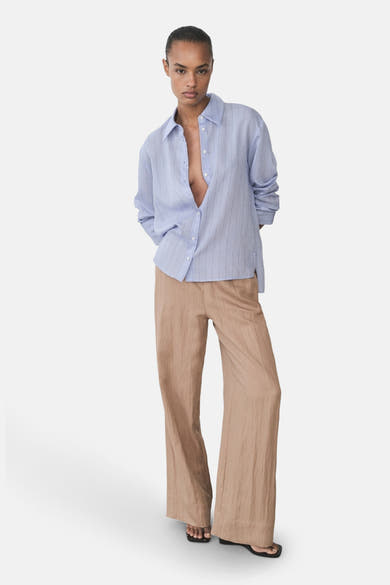 Bruine broek van MANGO, wijd en vloeiend, gedragen met zwarte sandalen met vierkante neus.