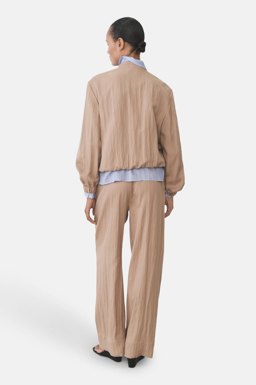 Bruine broek van MANGO, wijde en vloeiende stijl, gecombineerd met een lichtblauw overhemd en zwarte sandalen.