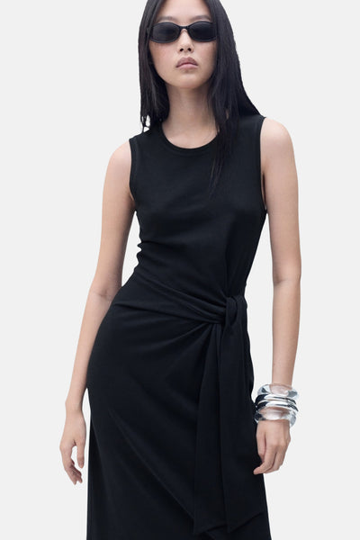 Zwarte jurk van MANGO, met een strikceintuur, gedragen met zilveren armbanden en een zwarte zonnebril.