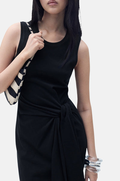 Zwarte jurk met strik in de taille van MANGO, gedragen met een zwart-witte gestreepte tas.