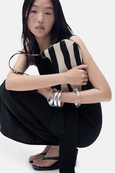 Robe noire de MANGO, portée par une femme accroupie avec un sac à rayures et des bracelets transparents.
