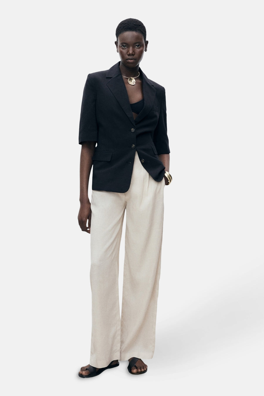 Beige broek van MANGO, wijd en vloeiend, gedragen met een zwarte blazer en sandalen.
