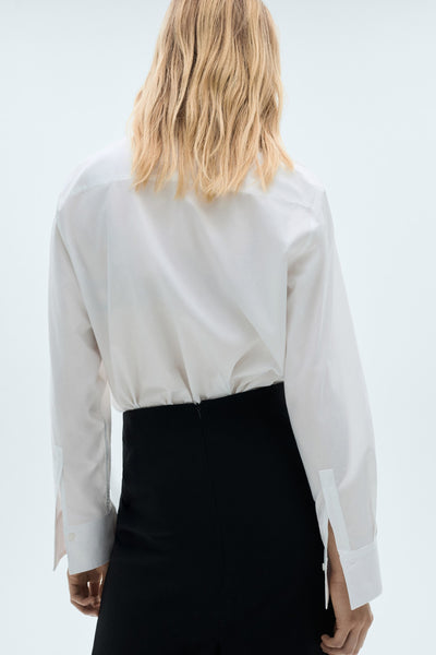 Chemise blanche à manches longues de MANGO, vue de dos avec une jupe noire taille haute.
