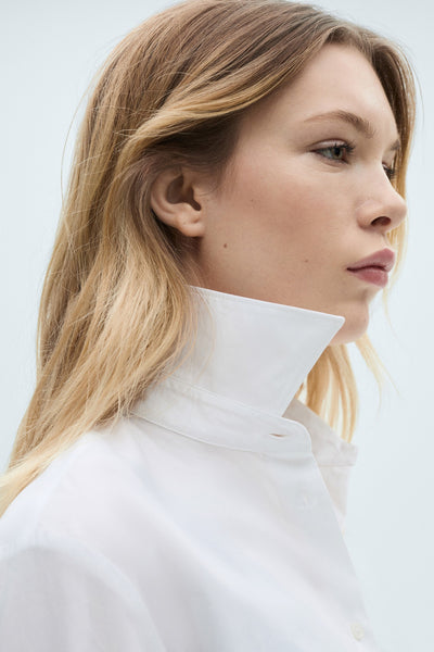 Chemise blanche à manches longues de MANGO, avec un col montant rigide, portée par un mannequin de profil.
