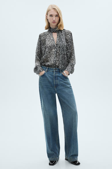 Grijze blouse met lange mouwen van MANGO, met een abstract patroon, gedragen met een wijde blauwe jeans en zwarte lakleren schoenen.
