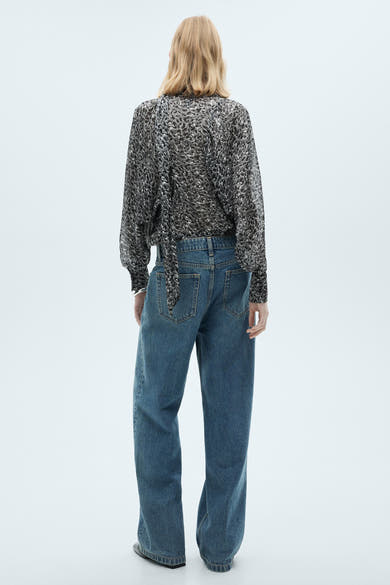 Grijze blouse met lange mouwen van MANGO, met gespikkeld patroon en strik aan de achterkant, gedragen met een blauwe jeans.