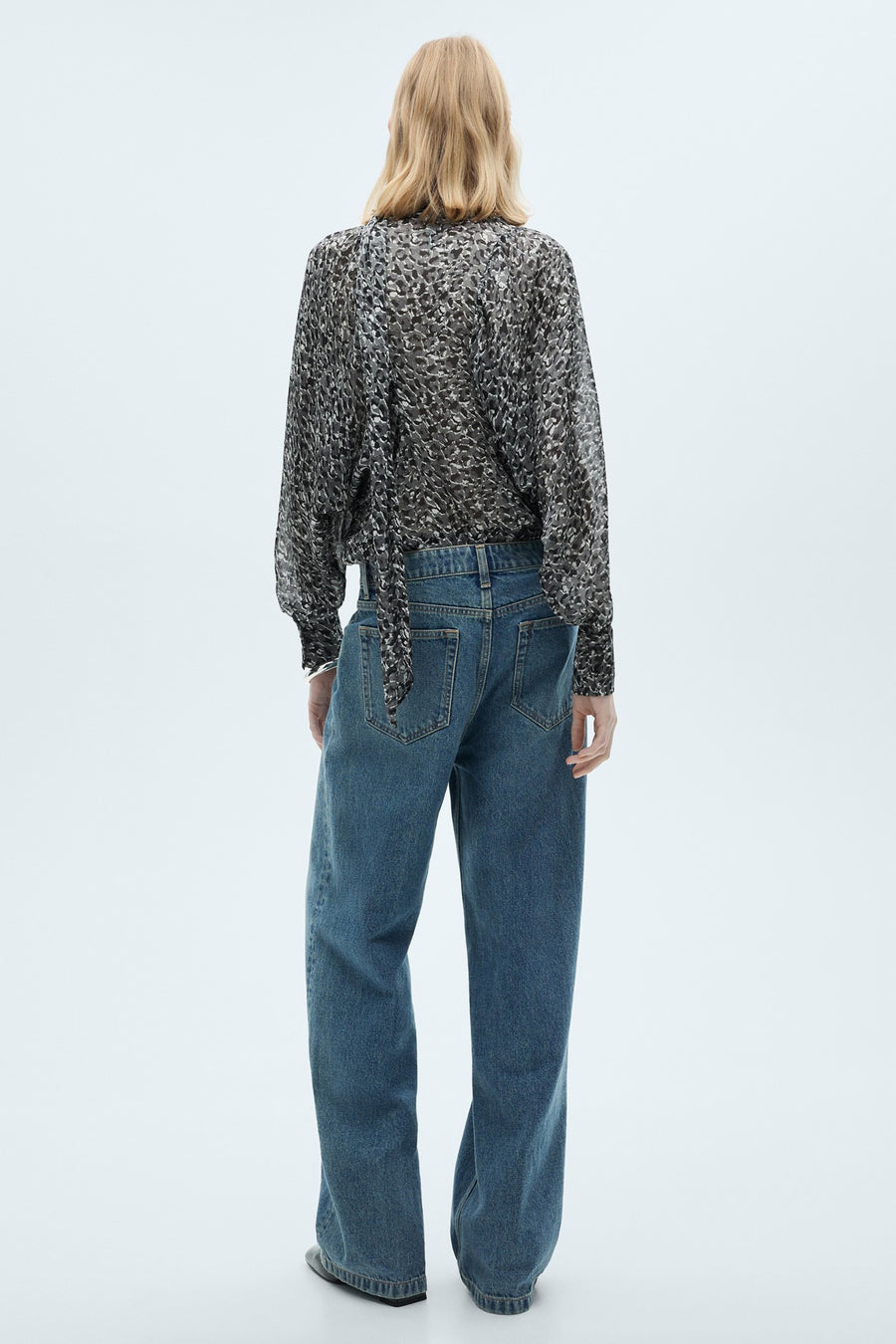 Grijze blouse met lange mouwen van MANGO, met gespikkeld patroon en strik aan de achterkant, gedragen met een blauwe jeans.