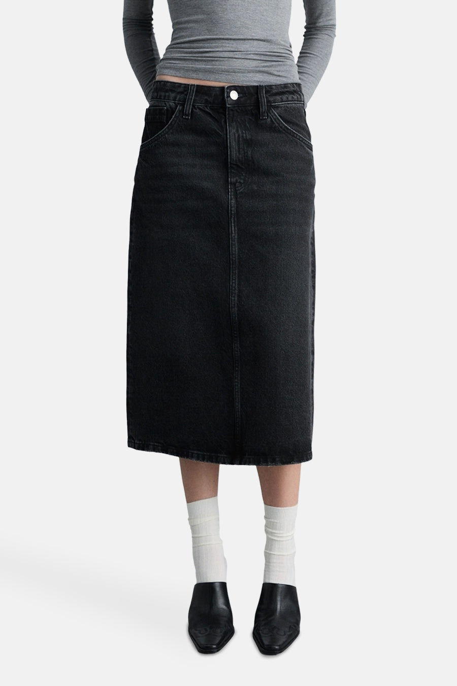 Zwarte midi-spijkerrok van MANGO, van achteren gezien, met zakken en een split aan de achterkant, gedragen met een grijze top en muiltjes.