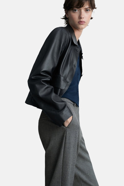 Pantalon gris de MANGO, porté avec une veste en cuir noire et un cardigan bleu marine, en vue latérale.