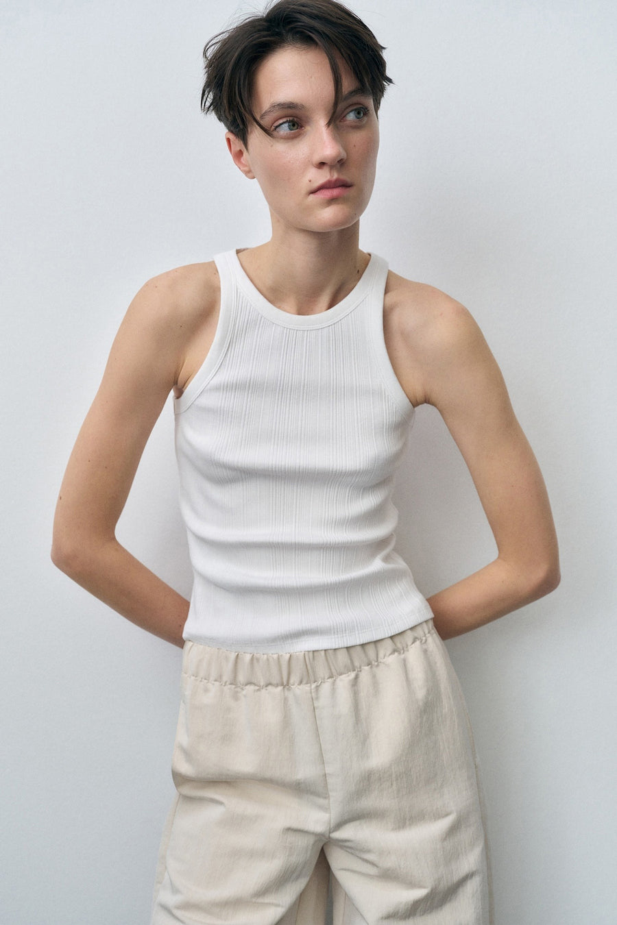 Débardeur blanc de MANGO, en maille côtelée, porté avec un pantalon taille élastique de couleur crème.
