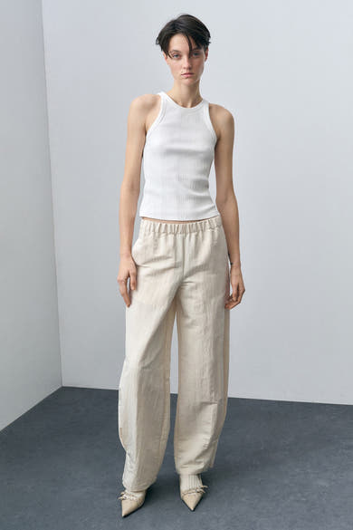 Witte geribbelde tanktop van MANGO, gedragen met een beige wijde broek en puntige schoenen.