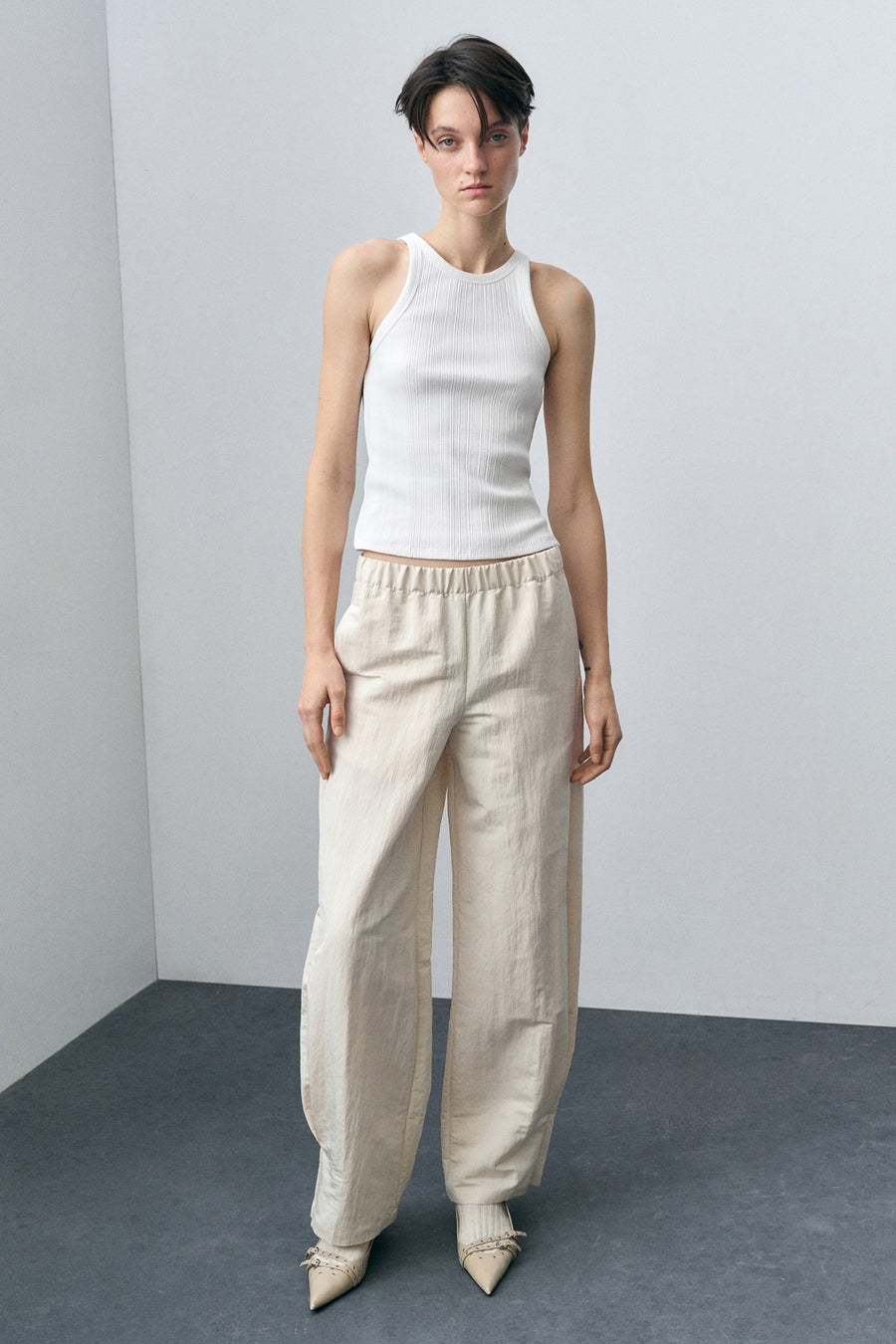 Witte geribbelde tanktop van MANGO, gedragen met een beige wijde broek en puntige schoenen.