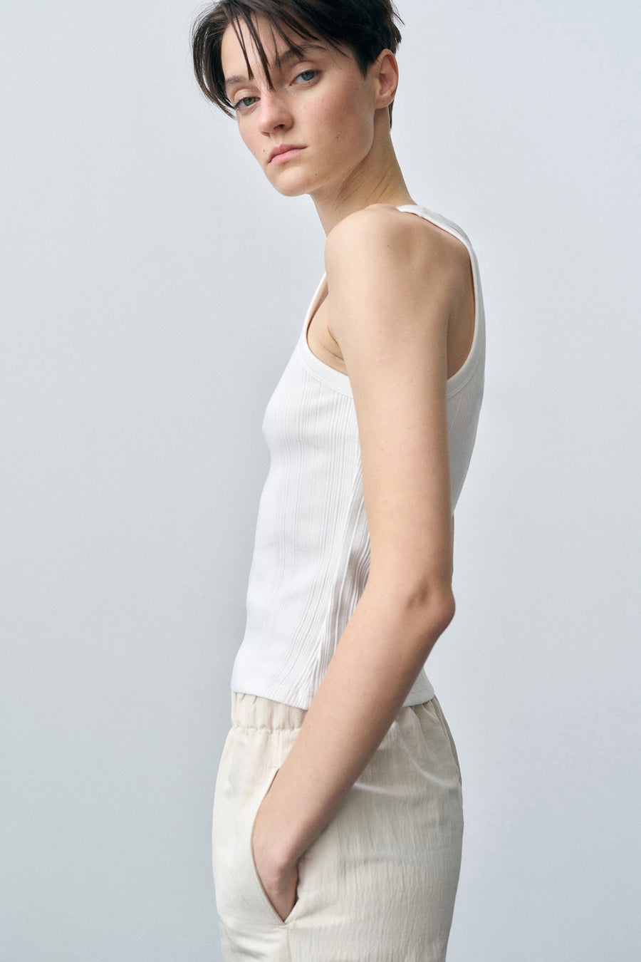 Witte geribbelde tanktop van MANGO, gedragen met een lichte broek met elastische tailleband, zijaanzicht.