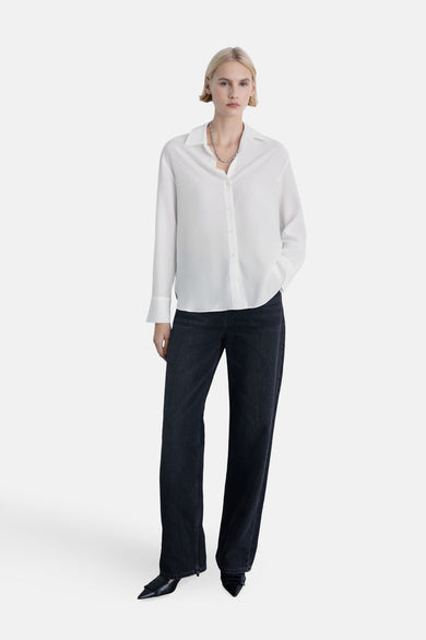 Witte lange mouw chemise van MANGO, gedragen met een donkere broek en hakken.