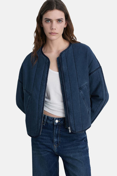 Kort jasje van middieblauw denim van MANGO, met ritssluiting en doorgestikte details, gedragen over een witte tanktop en een high-waisted jeans.