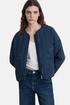 Kort jasje van middieblauw denim van MANGO, met ritssluiting en doorgestikte details, gedragen over een witte tanktop en een high-waisted jeans.