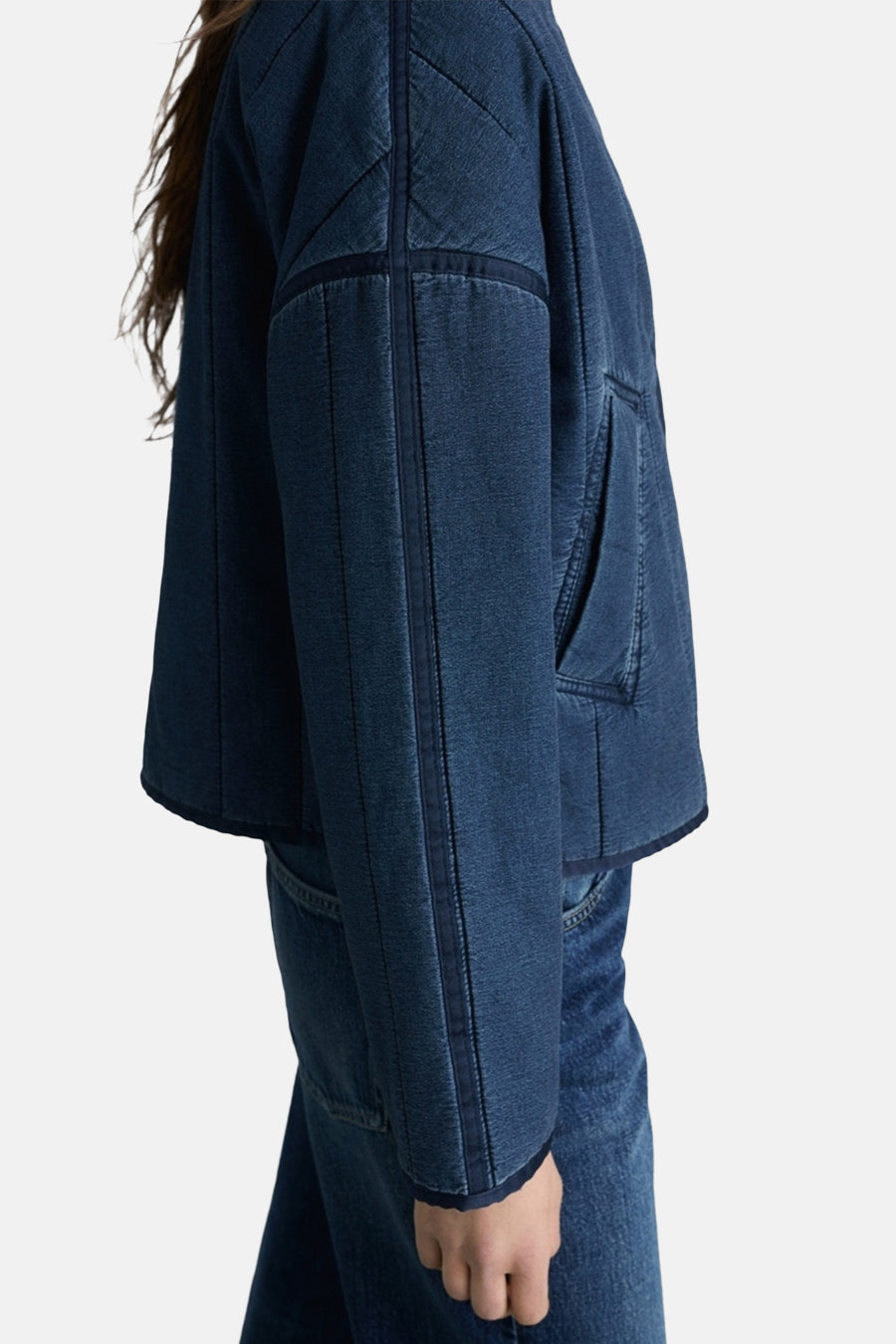 Korte spijkerjas in middieblauw van MANGO, met doorgestikte details en opgestikte zakken, zijwaarts bekeken.
