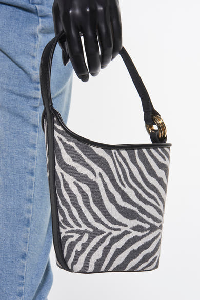 Sac à bandoulière noir de MANGO avec un motif zèbre, porté par une main gantée noire et des jeans bleus.