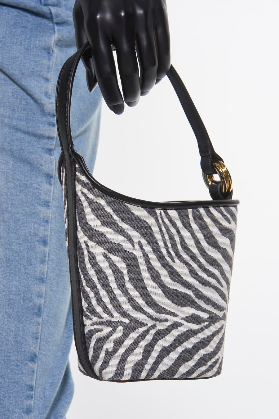 Sac à bandoulière noir de MANGO avec un motif zèbre, porté par une main gantée noire et des jeans bleus.