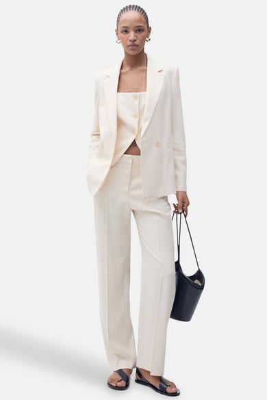 Pantalon de costume beige de MANGO, porté avec un tailleur et des sandales noires.
