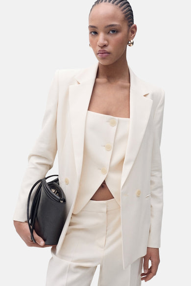 Pantalon de costume beige de MANGO, porté avec un blazer et un top coordonnés, avec un sac à main noir.
