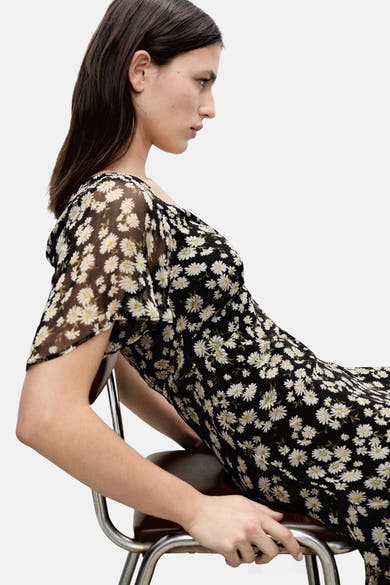Robe noire à manches courtes de MANGO, imprimé floral marguerite, portée par une femme assise de profil.
