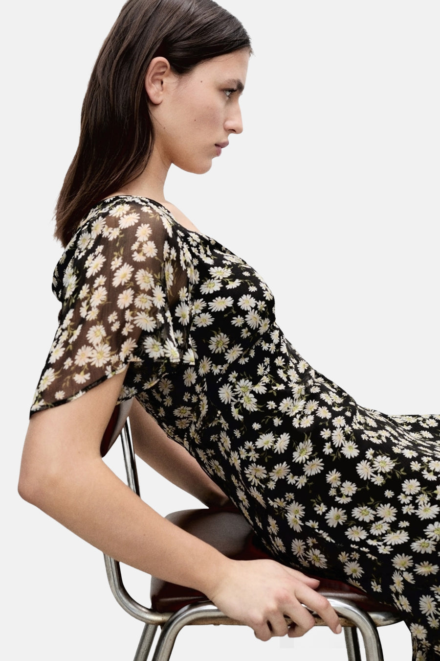 Robe noire à manches courtes de MANGO, imprimé floral marguerite, portée par une femme assise de profil.
