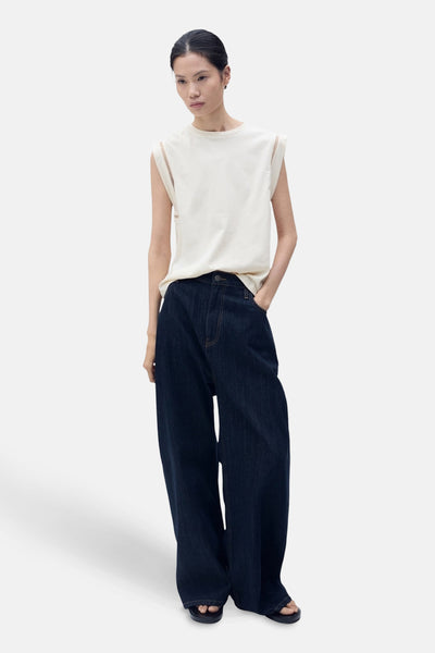 Top sans manches beige de MANGO, avec découpes aux épaules, porté avec un jean large bleu foncé.