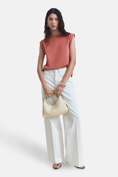 Roze mouwloze top van MANGO, gedragen met een witte broek met hoge taille en een handtas van gevlochten stro.