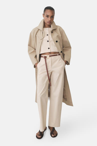 Pantalon écru de MANGO, porté avec une ceinture fine marron, et un trench coat beige.