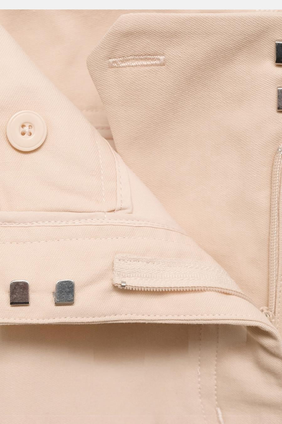 Pantalon écru de MANGO, fermeture à glissière et bouton visible, détail de couleur unie.