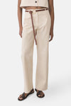 Pantalon écru de MANGO, avec une ceinture fine marron nouée, porté avec des sandales en cuir foncé.