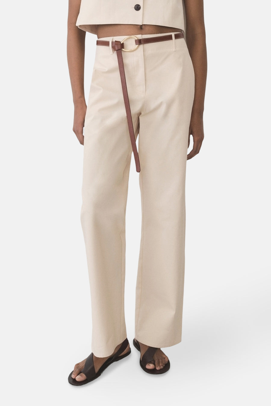 Pantalon écru de MANGO, avec une ceinture fine marron nouée, porté avec des sandales en cuir foncé.