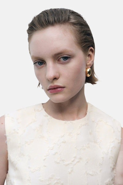 Ecru mouwloos blouse van MANGO, met een delicaat textuurpatroon op een gebroken witte achtergrond.