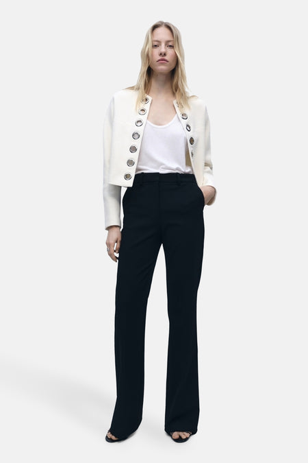 Witte blazer van MANGO met decoratieve metalen oogjes, gedragen over een witte tanktop en een zwarte broek.