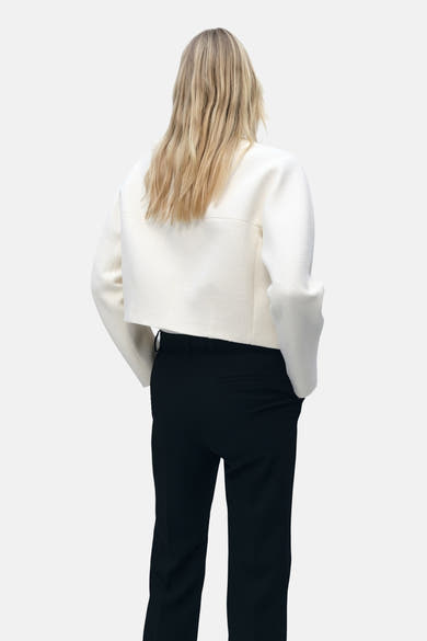 Blazer blanc cassé de MANGO, coupe courte avec texture à chevrons, porté avec un pantalon noir taille haute.