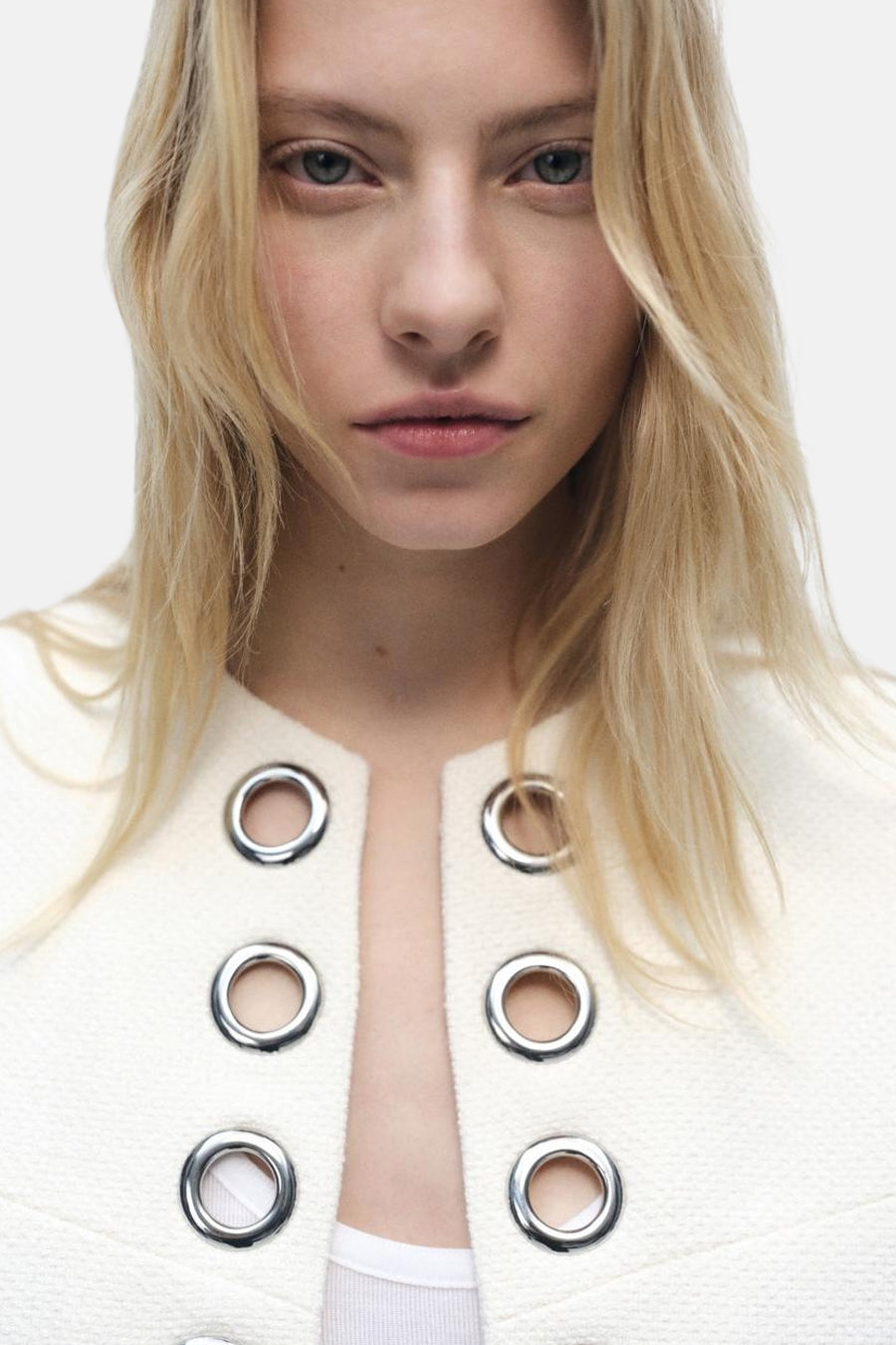 Blazer blanc de MANGO avec oeillets décoratifs argentés et texture tweed.