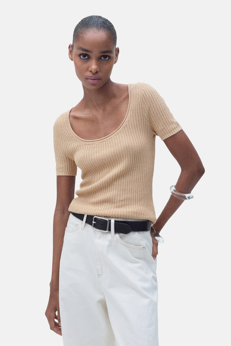 Pull à col rond beige de MANGO, en maille côtelée, porté avec un jean blanc taille haute et une ceinture noire.