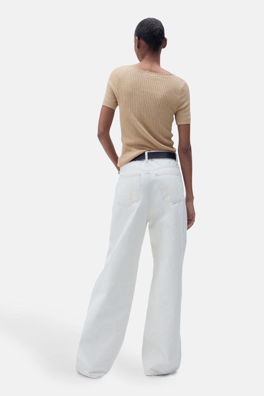 Pull à col rond beige de MANGO, porté avec un pantalon blanc taille haute et une ceinture noire.