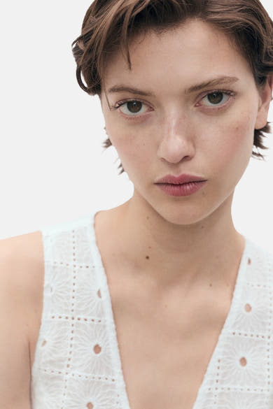 Blouse blanche sans manches de MANGO, avec broderie anglaise florale ajourée sur un tissu texturé.
