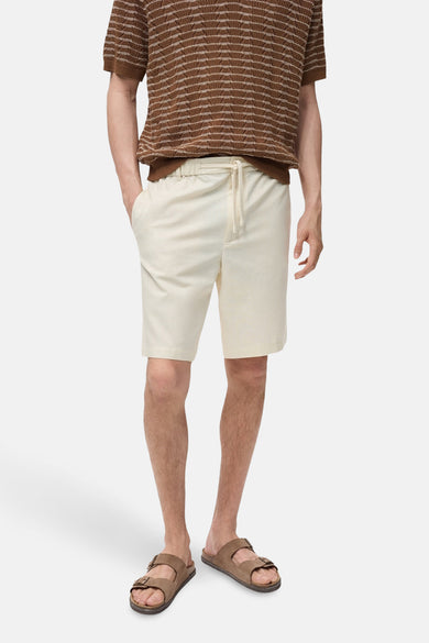 Ecru short van MANGO, met een achterzak, gedragen met een gestreept poloshirt en bruine sandalen.