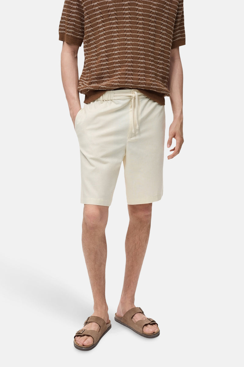 Ecru short van MANGO, met een achterzak, gedragen met een gestreept poloshirt en bruine sandalen.