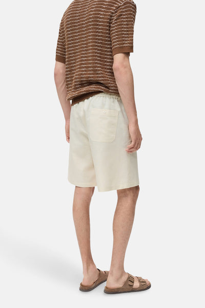 Short écru de MANGO, avec une poche arrière, porté avec un polo rayé et des sandales marron.
