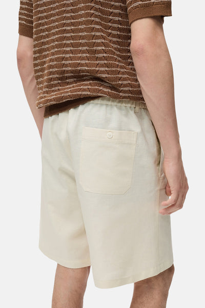 Short écru de MANGO, avec une poche arrière boutonnée, porté avec un pull en maille marron.